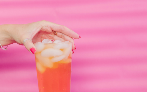 hand holding drink with pink backdrop