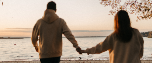 couple holding hands walking towards beach
